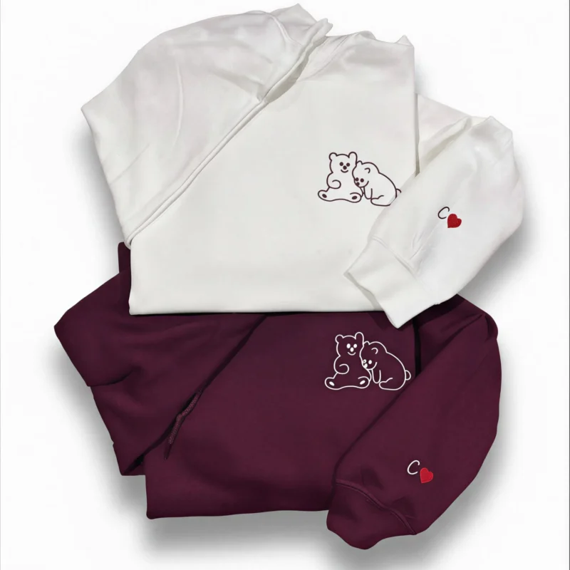 White sweatshirt on top of a maroon one, both with a hugging bears outline on the chest and a heart on the sleeve