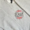 Close-up of the BEST Dad EVER badge embroidery: red letters and stars around Dad in dark grey script