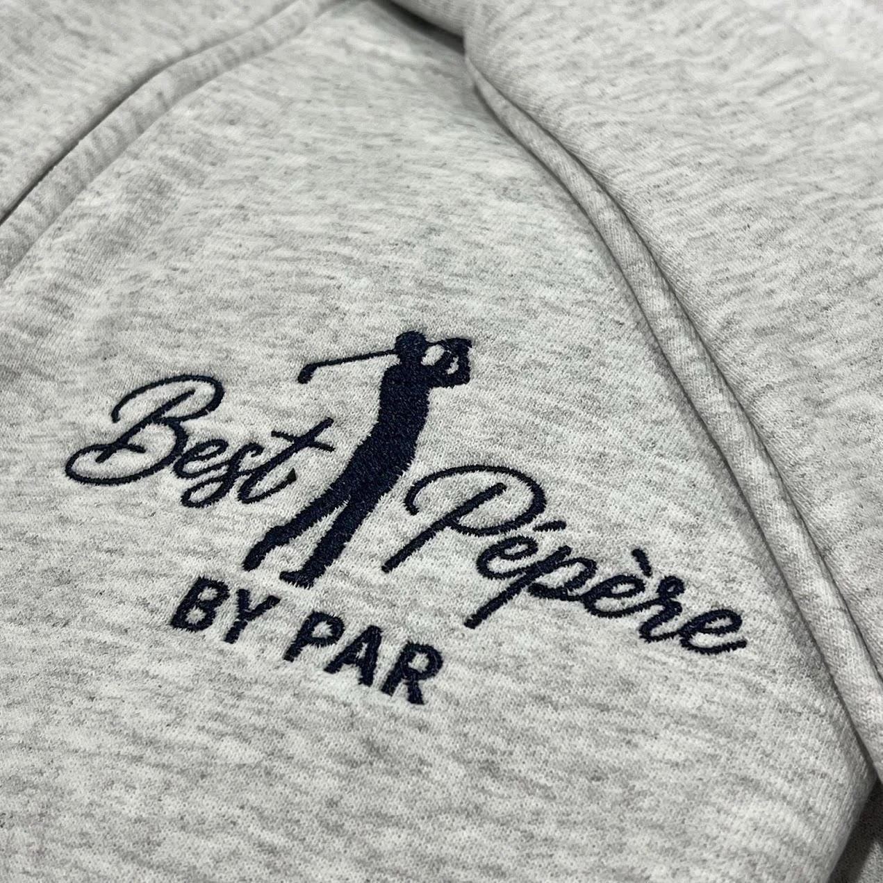 Angled close-up of the navy golfer embroidery with Best Pépère in script and BY PAR on heather grey fleece