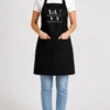 Woman wearing a black apron with front pockets and an embroidered white business logo on the bib