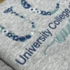 Grey sweatshirt with navy floral school letters, the college name in navy and nursing in teal script