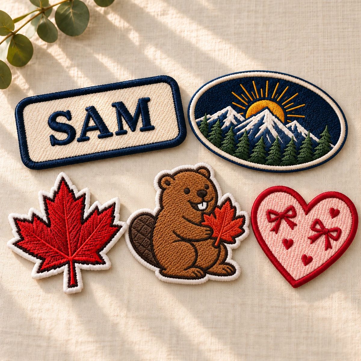 Custom embroidered patches with satin borders: a SAM name patch, a mountain oval, a maple leaf, a beaver holding a maple leaf and a pink heart