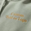 Close-up of Custom Text or Logo embroidered in gold serif thread on sage green hoodie fleece