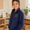 Educator standing in a classroom in a navy quarter-zip with a name and ECE credential on the left chest