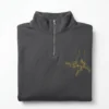 Folded charcoal quarter-zip sweatshirt with the gold family fist bump line art and names on the left chest