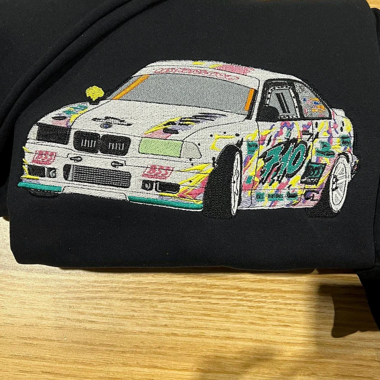 White sports car embroidered in the graffiti street art style, with pink, yellow and teal splashes and the number 710, on a black hoodie