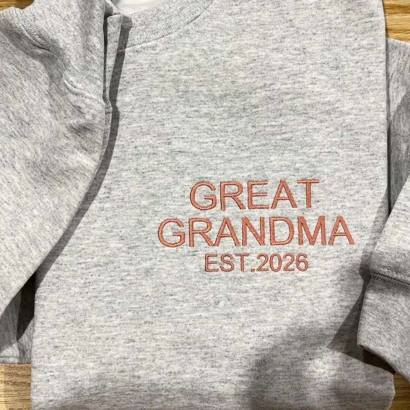 Ash grey sweatshirt with GREAT GRANDMA and EST.2026 stacked in coral sans-serif capitals on the chest