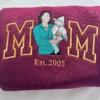 Maroon sweatshirt with gold outline M M around a portrait of a mom holding her baby, Est. 2005 below