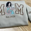 Sand sweatshirt with a mom and baby portrait in MOM lettering, Est. 2026, and the name Alyana with a heart on the sleeve
