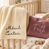 Ivory blanket with Mikail Carter and mauve blanket with Faith hanging over a wooden crib rail