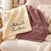 Ivory and mauve baby blankets with embroidered script names draped over a nursery armchair with a plush bunny