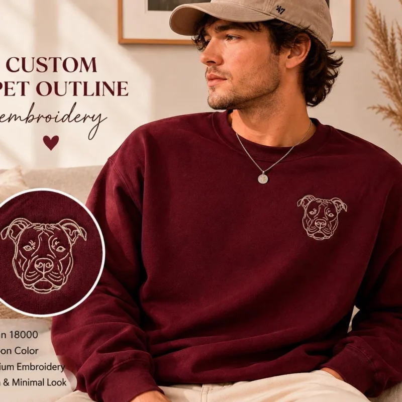 Pet outline embroidery shown on a maroon sweatshirt: a cream single-line dog face on the left chest, with a close-up inset