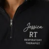 Close-up of a black quarter-zip with Jessica in white script, RT and RESPIRATORY THERAPIST on the left chest