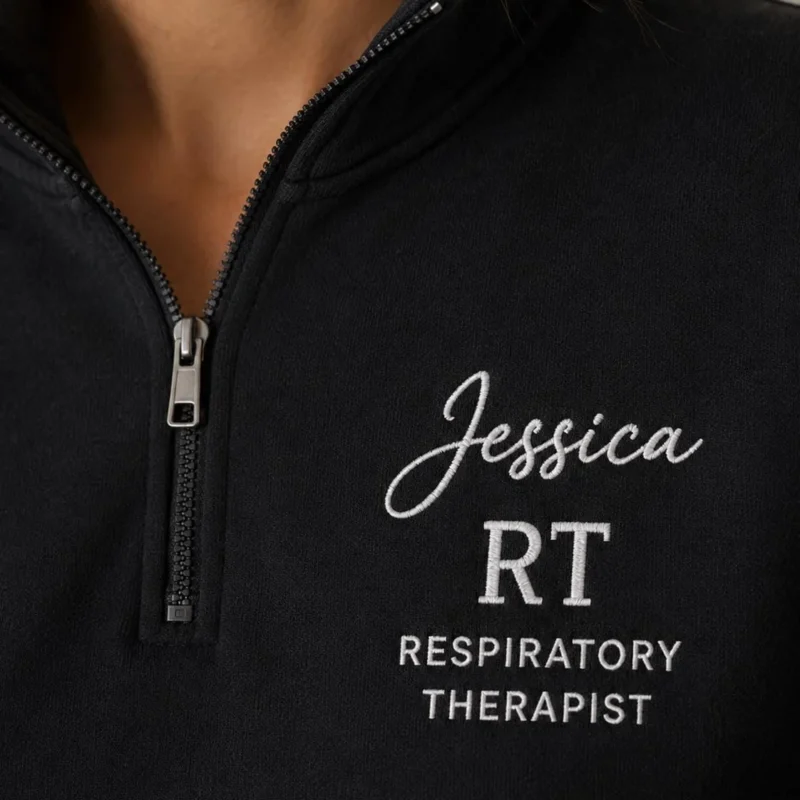 Close-up of a black quarter-zip with Jessica in white script, RT and RESPIRATORY THERAPIST on the left chest