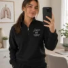 Woman taking a mirror selfie in a black quarter-zip embroidered with her name, RT and Respiratory Therapist
