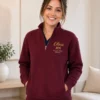 Nurse in navy scrubs and a maroon quarter-zip with her name and RN credential embroidered on the left chest