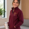 Smiling nurse holding a tumbler, wearing a maroon quarter-zip with gold name and RN embroidery