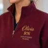 Close-up of a maroon quarter-zip with Olivia in gold script, RN in gold and REGISTERED NURSE in small capitals