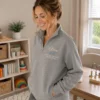 Woman in a therapy room wearing a grey quarter-zip with Olivia, SLP and Speech Language Pathologist stitched