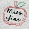 Close-up of a red outline apple with a green leaf framing the name Miss. Jini in black script embroidery