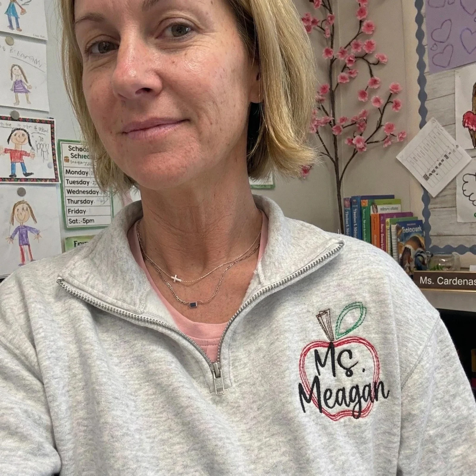 Teacher in a classroom wearing an ash quarter-zip with an embroidered apple and Ms. Meagan on the left chest