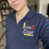 Teacher wearing a navy quarter-zip with Miss. Lizze, a red apple, ruler and pencil stitched on the left chest