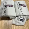 Stacked sand hoodies showing the couple portrait, names joined by a heart and the wedding date in black