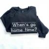 Black sweatshirt flat-lay with When's go home time? stitched in white school-style letters across the chest