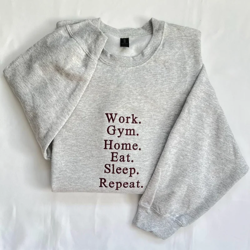 Ash grey sweatshirt with Work. Gym. Home. Eat. Sleep. Repeat. stacked in maroon serif embroidery, flat-lay