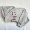 Ash grey crewneck folded with sleeves crossed and the six-word maroon routine quote on the chest